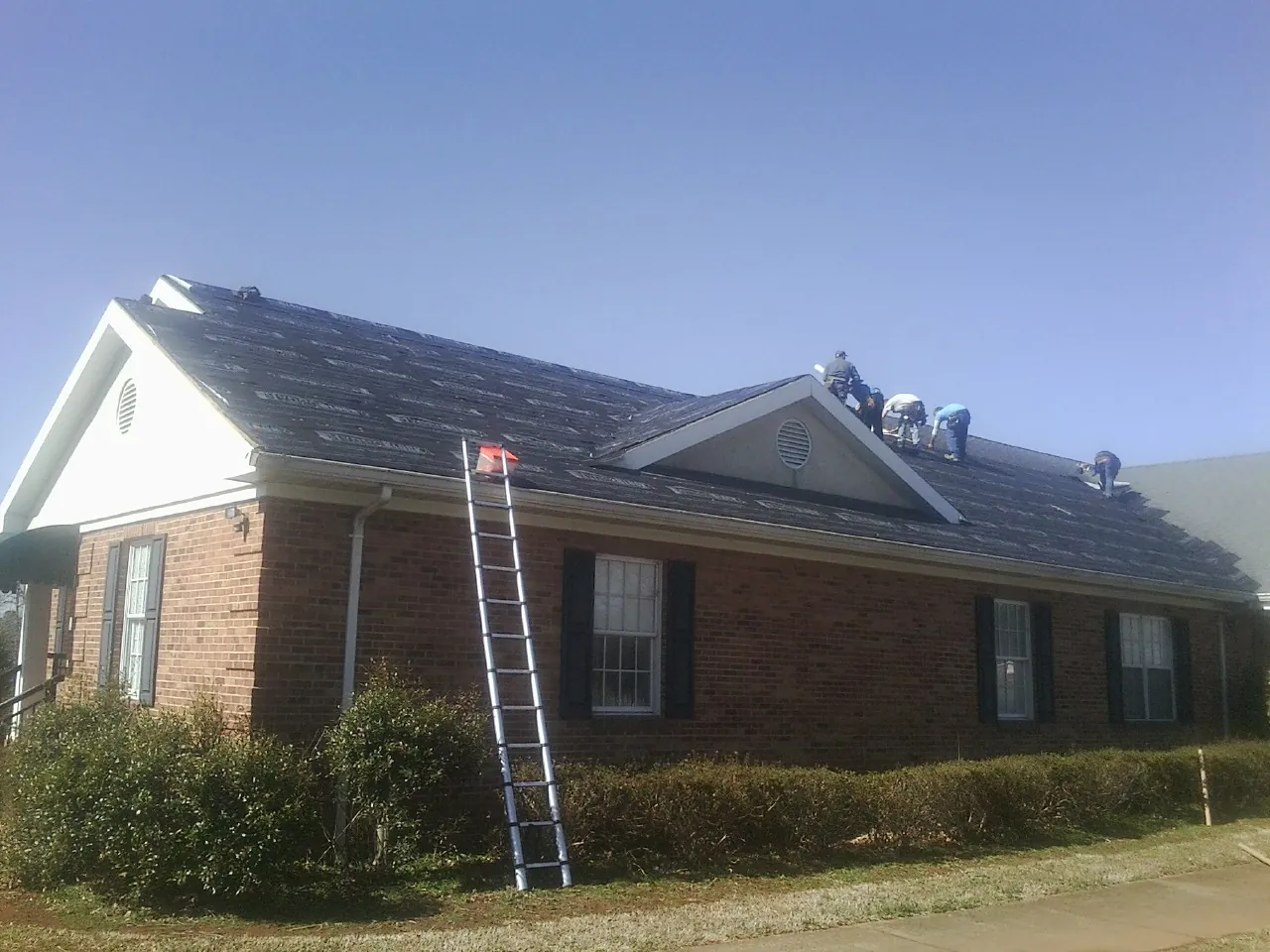 Crew tearing shingles off a brick ranch roof with a ladder set — Metal Roof Repair work by our crew in Nanticoke