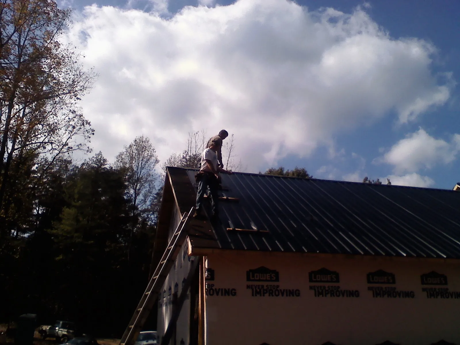 Roofer fastening dark metal panels high against a cloudy sky, from a Roof Inspection job in Nanticoke